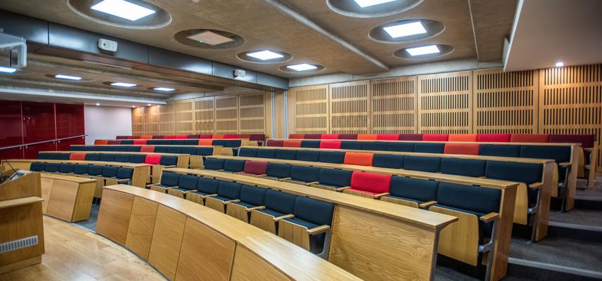 A large modern lecture room, with cushioned seats arranged in curved rows behind wooden desks.