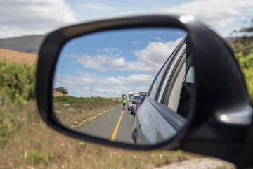 A close-up of a car wing mirror, which is reflecting a queue of traffic being monitored by someone in a high-vis jacket.