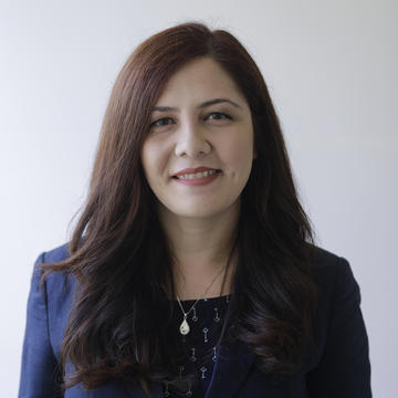 Professor Govella has long dark hair. She is wearing a navy dress and blazer. 