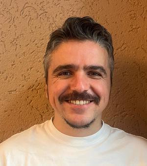 Dr Belder has short dark hair and is wearing a white t-shirt. He is smiling at the camera.