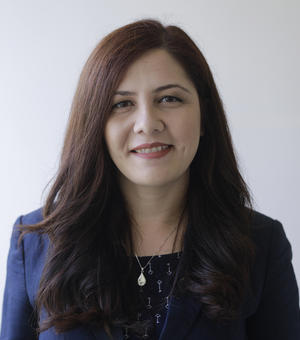 Professor Govella has long dark hair. She is wearing a navy dress and blazer. 