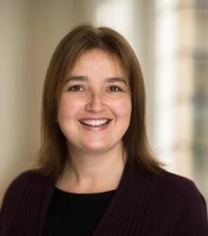Rachel Barber has shoulder-length brown hair. She is wearing a black top and blazer, smiling at the camera.