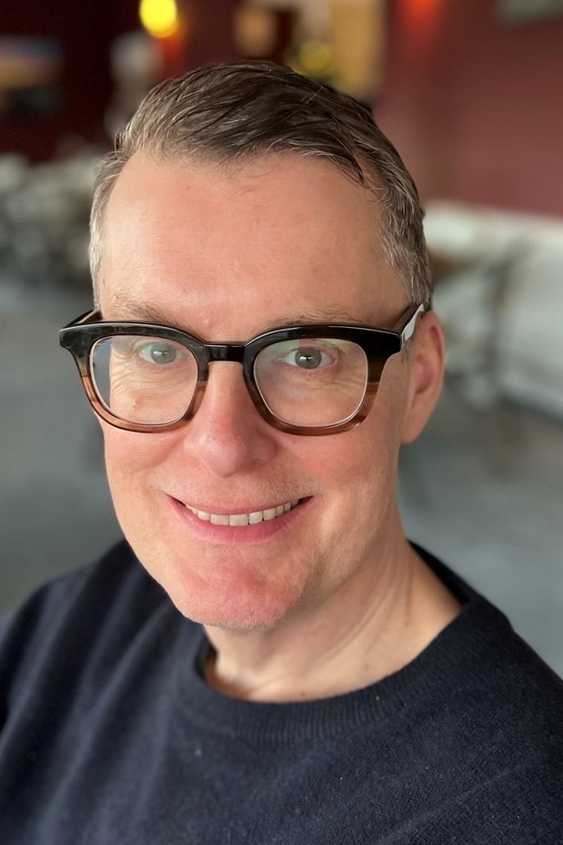 Professor paul chaisty has short dark grey hair, glasses and is smiling at the camera. He's wearing a black t shirt. 