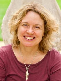 Rachel has shoulder-length blonde wavy hair and is smiling at the camera. She's wearing a ruby coloured top with silver pendant necklace