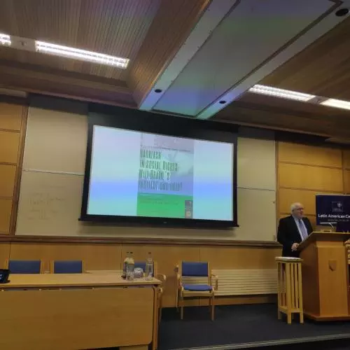 Professor Timothy Power stands on stage, in front of a projected presentation. 2019