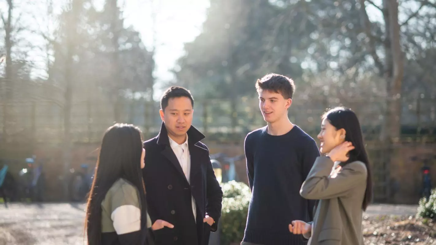 Three students standing outside chatting with a tutor. Photo credit: John Cairns Photography