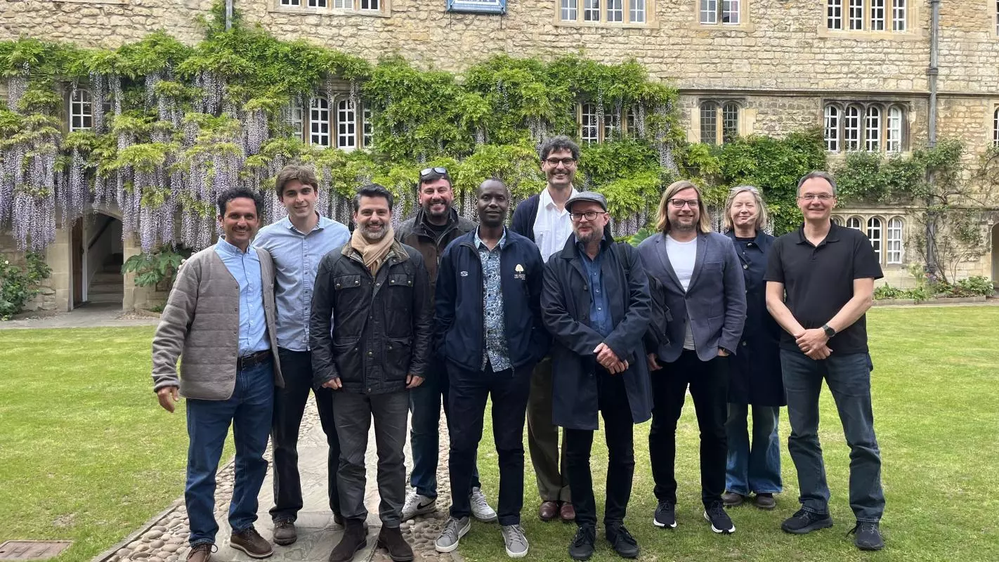Felip Krause has dark hair, grey beard and is wearing a jacket and black jeans. He's standing with a group of ten people in a college garden.