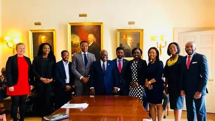 ghanas president and other people in suits standing alongside a large wooden table. Everyone is smiling at the camera. 