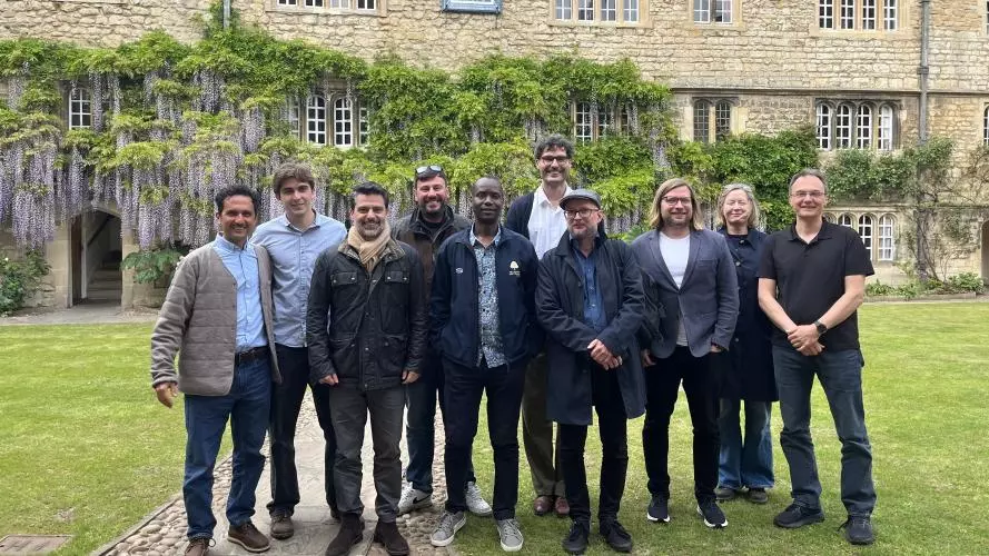 Felip Krause has dark hair, grey beard and is wearing a jacket and black jeans. He's standing with a group of ten people in a college garden.