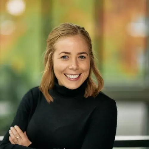 Dr Marnie Howlett has shoulder length blonde hair and is smiling broadly at the camera. She's wearing a black polo neck sweater. She has her arms folded in front of her.  