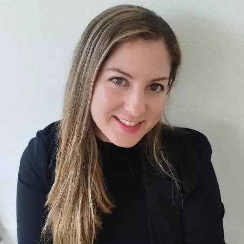 Dr Villegas Plá has long blonde hair. She is wearing a black top and blazer, looking upwards slightly at the camera and smiling. 