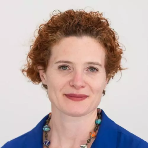 Anna Lora-Wainwright has curly auburn hair that she has tied back. She is wearing a royal blue shirt with a necklace made from various multicoloured beads. 
