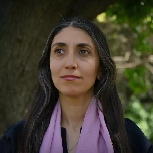 Dr Alice Gaya has long dark hair and is wearing a lilac scarf over a dark blouse. 