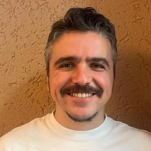 Dr Belder has short dark hair and is wearing a white t-shirt. He is smiling at the camera.