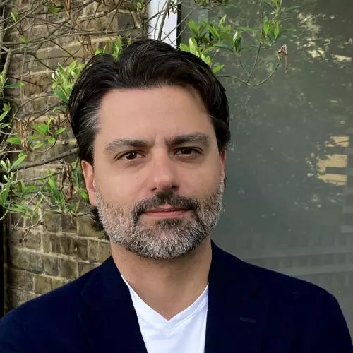 felipe krause has short dark hair and a grey beard. He's wearing a white t shirt under a black jacket