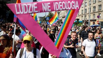 A crowd of people walking down a street holding rainbow flags and a pink triangle with the text 'LUDZIE, NIE IDEOLOGIA'. 