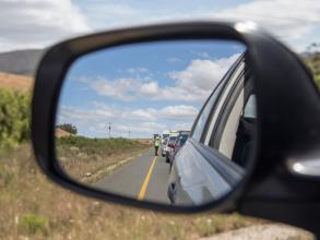 A close-up of a car wing mirror, which is reflecting a queue of traffic being monitored by someone in a high-vis jacket.