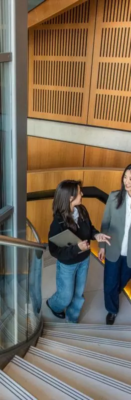 Two students seen from above walking up a wide, modern spiral staircase